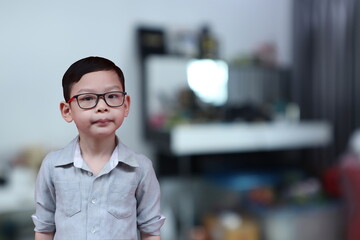 an asian young boy wearing glasses and long sleeve shirt is standing in his small bedroom in the morning