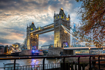 Autumn sunrise view to the illuminated Tower Bridge of London, United Kingdom, with a tree with golden leafs in front
