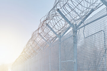 Restricted area fence against blue sky closeup. Barbed wire. Classified state zone. Migration...