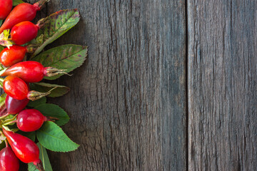 Ripe wild rose with foliage on a wooden table. Rustic background with medicinal plant