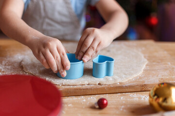 A little boy in a blue shirt makes New Year's gingerbread. Making cookies using a cookie cutter. New Year and Christmas concept.