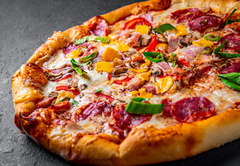 Pizza with Mozzarella cheese, salami, chicken meat, beef, ham, Tomato sauce, pepper, spices. Italian pizza on Dark grey black slate background