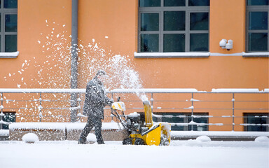 Worker with track drive snow blower removing deep snow, heavy duty assistant for snow and ice...