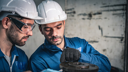 Two industrial workers inspecting a gear piece in the factory. Quality control management.	
