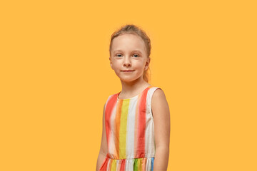 Portrait of a beautiful sweet smiling girl in a dress with bright stripes. Orange isolated background.