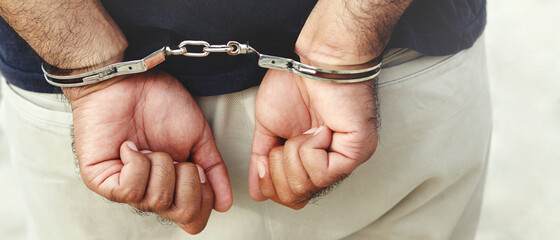 Prisoner male criminal standing in handcuffs with hands behind back. banner copy space. 