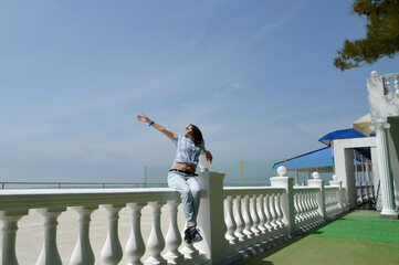 A girl sits on the railing on the black sea embankment on a clear day.