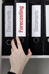 Forecasting. File Folder is taking by a hand from office shelf. Red Text is on the label of the...