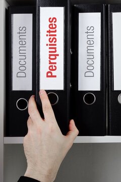 Perquisites. File Folder is taking by a hand from office shelf. Red Text is on the label of the documents.