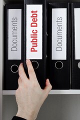 Public Debt. File Folder is taking by a hand from office shelf. Red Text is on the label of the...