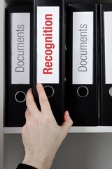 Recognition. File Folder is taking by a hand from office shelf. Red Text is on the label of the...