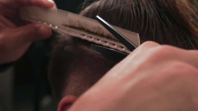 Barber cuts a man's hair using scissors and a comb in a barbershop. Close up.