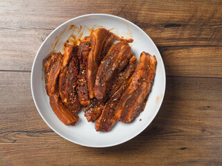 Raw pork belly slices in Korean style marinade on a white plate.