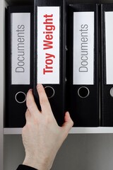 Troy Weight. File Folder is taking by a hand from office shelf. Red Text is on the label of the...