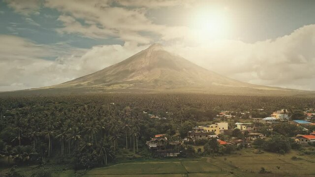 Sun cityscape of rural town at green volcano valley aerial. Contryside city streets at hillside greenery dale of Mayon mount, Philippines. Houses, cottages at tropic palm trees, plants. Road with cars