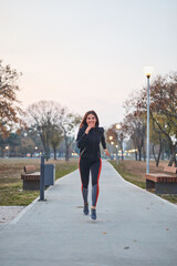 Smiling sporty young woman running in urban park.