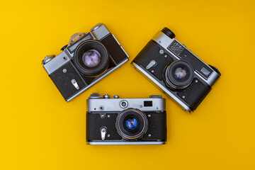 Three old film cameras lie on a yellow background in the shape of a triangle