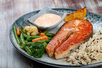 Salmon steak with cheese sauce, blanched vegetables and wild rice