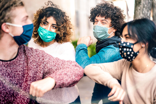 Multiracial friends greeting with elbow bump wearing face protection - New normal lifestyle concept with young people covered by disposable mask - Selective focus on middle left woman - Powered by Adobe
