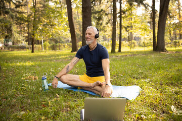 Calm mature male doing meditation in headphones outdoors