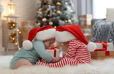 Cute children in Santa hats on floor in room with Christmas tree