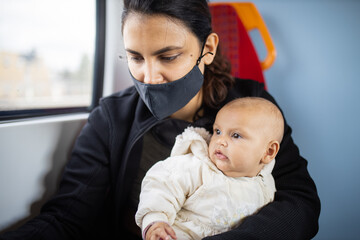 Woman sitting next to a window in a bus and holding her baby in her arms