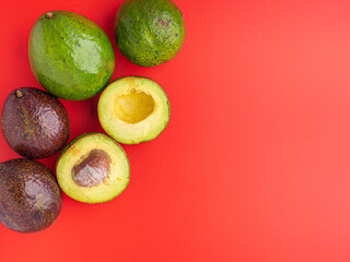 Organic avocado with seed, avocado halves and whole fruits on red background. Top view. Green avocados pattern in minimal flat lay style. Space for text. Concept of healthy fruit