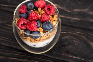 delicious granola with berries and yogurt in glass cup on wooden surface