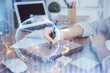 Double exposure of hands making notes with world map hologram and data theme icons. Concept of international network data.