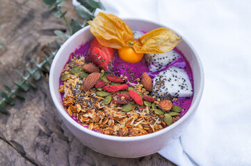 Purple smoothie bowl: Dragon fruit smoothie with banana, coconut, almonds, sunflower and chia seeds and strawberry