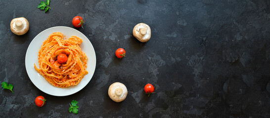 Fototapeta na wymiar Pasta in a white plate. Pasta with tomato sauce, mushrooms with cherry tomatoes. Dark background. View from above. Free space for text. Copyspace