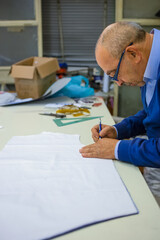 Old tailor prepares paper models in his workshop. Concept of manual work linked to professional knowledge and craftsmanship