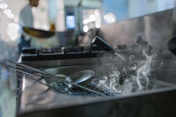 View on a ladle and container for cooking and frying. In the background the kitchen of the restaurant. Selective focus