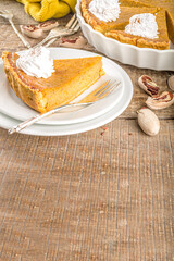 Traditional Autumn Pumpkin Pie. Homemade American Pumpkin pie topped with Whipped Cream. Rustic wooden table bakcground with Cozy plaid and sweater.