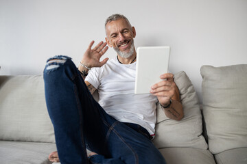 Cheerful man waving at a tablet camera