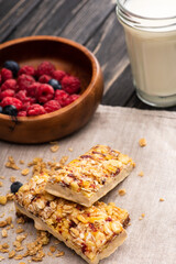 delicious muesli bars on napkin with blurred glass of milk and berries on background