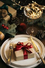 Christmas table setting with gift box on the plate on wooden table. Concept of Christmas and New Year dinner.