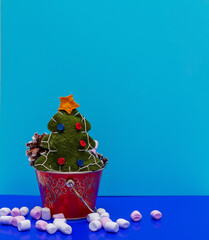 Christmas composition. Green felt tree, pink and white marshmallows and cones on a blue background. Copy space. New Year 2021. Handmade.
