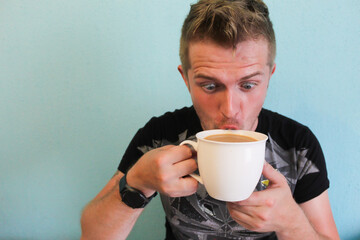 Young handsome man addicted to coffee. Coffeemania. Man drinking coffee funny