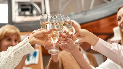 A group of women of different age and nationalities standing clinking glasses of champagne standing together