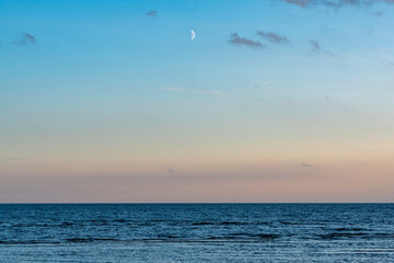 Blick auf die ruhige See am Abend. Der Mond ist zu sehen.