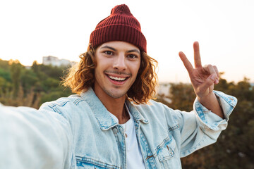 Cheerful young curly man taking a selfie by camera