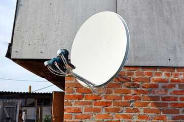 Satellite dish is attached to the wall of the house. A domestic satellite tv installation under roof