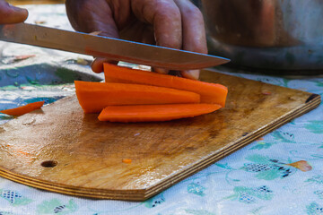 Closeup of hands slicing carrots on chopping board. Closeup of hands cutting vegetables in kitchen. Detail of man chopping vegetables for a recipe at home.