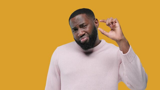 Young handsome black man show something small: Little bit Gesture. on yellow background