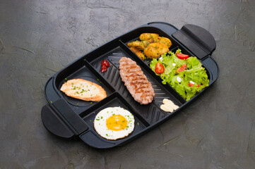 Breakfast, fried steak or cutlet, salad with tomato and green vegetables, toast, potatoes, egg on black plate. The concept of a healthy diet, diet, menu, high-grade lunch