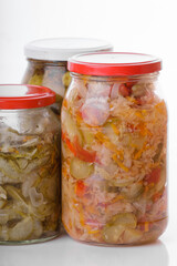 Glass jars of pickled homemade organic cucumber carrrot with garlic and red cabbage vegetables  isolated on white background 