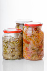 Glass jars of pickled homemade organic cucumber carrrot with garlic and red cabbage vegetables  isolated on white background 