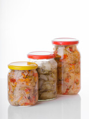 Glass jars of pickled homemade organic cucumber carrrot with garlic and red cabbage vegetables  isolated on white background 