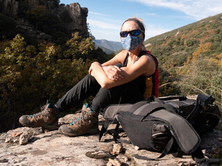 BLOND WOMAN HIKING WITH GLASSES AND MASK SITTING IN THE MOUNTAIN